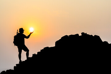 Silhouette of young male tourists Stand and watch the beautiful sunset on top of the mountain with your backpack.