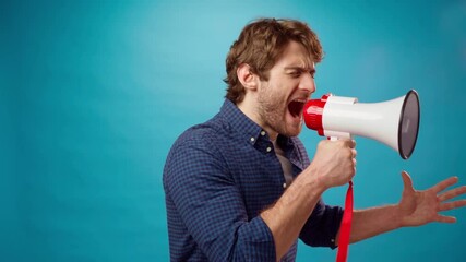 Irritated bearded young man screaming in megaphone against blue background - Powered by Adobe