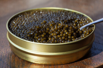Black beluga caviar, sturgeon in a metal can on a wooden table. Close-up, blur, soft focus, selective focus.