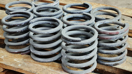Group of steel springs of shock absorbers on wooden palete. Spare parts of heavy industrial machinery.