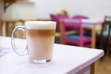 A transparent mug with cappuccino coffee is on the table in the kitchen. Homemade coffee concept. Copyspace.