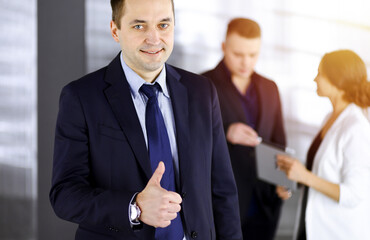 Portrait of a successful middle aged businessman, who is enjoying a good result of a teamwork, while standing at meeting in a sunny office. Concept of business success