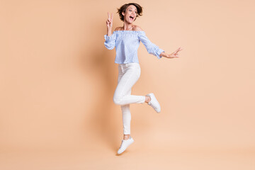 Fototapeta na wymiar Full length body size view of lovely cheerful girl jumping having fun showing v-sign isolated over beige pastel color background