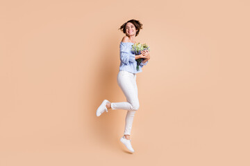 Fototapeta na wymiar Full length photo of young excited girl happy embrace flowers bouquet jump look empty space isolated over beige color background