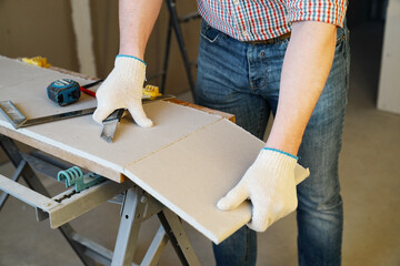 A man cuts a drywall sheet with a knife - obrazy, fototapety, plakaty