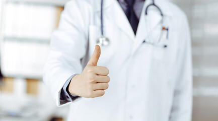Unknown male doctor standing with thumbs up sign in clinic near his working place, closeup. Perfect medical service in hospital. Medicine and healthcare concept
