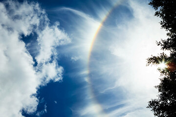 Summer rainbow above trees, with wispy clouds on a beautiful sunny day in July.