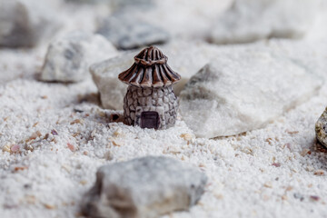 A miniature house and a landscape of white sand with stone and shells. Small toys.