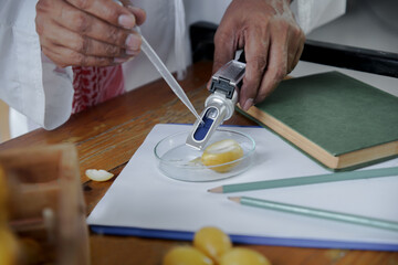 Selective focus of Arab senior's hand holding dropper to dropping liquid from date palm slices to Brix Refractometer for test sweetness level of sugar in fruits