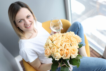 Smiling woman holding a glass of wine and a bouquet of flowers in her hands
