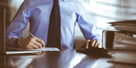 Unknown man accountant in blue shirt use calculator and computer with holding pen on while staying at home during covid pandemic. Taxes and audit concept