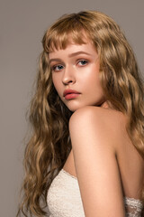 Close up portrait of young fashion model with beautiful natural blond wavy hair and gentle makeup. The concept of healthy clean well-groomed skin. Trendy hairstyle with bangs cut.