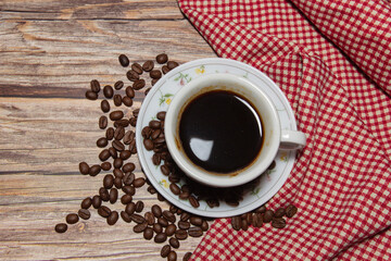 hot coffee cups and coffee beans with red patterned fabric on a wooden background.