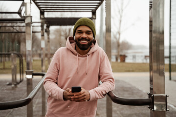 happy african american sportsman listening music in wireless earphones on sports ground