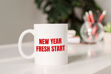 Coffee mug with text NEW YEAR FRESH START in workplace background.