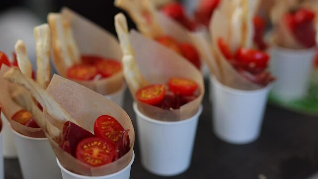 Sliced ​​jamon with fresh baguette and cherry tomatoes in a cardboard glass. Serving snacks at events. Buffet table.