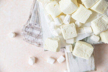 Yellow square shape marshmallow and white vanilla marshmallow on wooden cutting board, light concrete background. High key. Top view.
