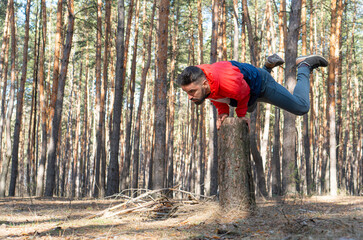 Pilates outdoors. Strong athletic man doing static strength exercises on a fresh air in the forest.