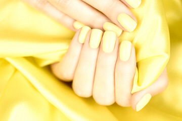 Female hands with yellow manicure on a yellow silk background.