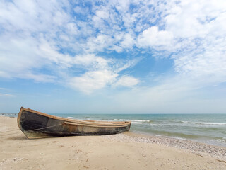 Old wooden boat on the sea shore, cloudy sky, sunny weather.