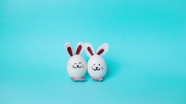 4k Two cute Easter bunnies made of white chicken eggs move and congratulate on holiday. Happy Easter Bunny Day Concept. Light blue background. Holiday greeting card. Stop motion animation. Copy space.