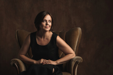Beautiful middle aged woman sitting in a brown velvet armchair