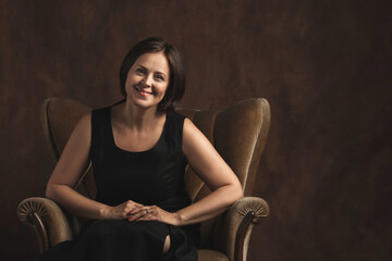 Beautiful middle aged woman sitting in a brown velvet armchair