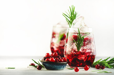 Cranberry cocktail or mocktail with ice, rosemary and red berries in tumbler glass, gray background, copy space