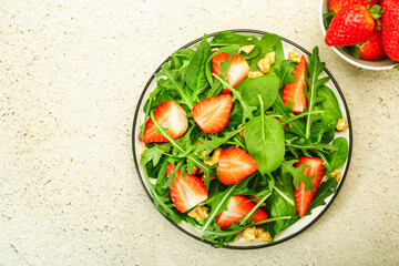 Summer Strawberry Salad. Spinach leaves, arugula, walnuts on gray background. Healthy food concept. Flat lay, top view