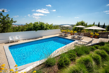 Outdoors shot of a clean pool with some loungers on the side on a clear sunny day.