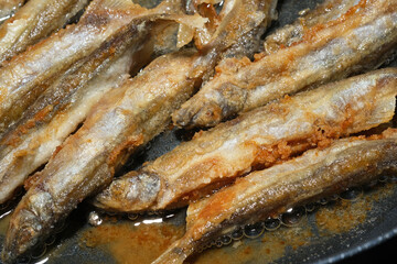 Fried fish in a frying pan. Capelin fried in oil with crispy breading.  Selective focus