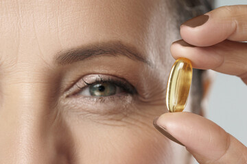 Middle aged woman holding capsule with a fish or krill oil source of Omega-3 fatty acids
