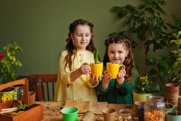 Two girls at a table with a planting pot and gardening tools. Children's watering and care of...