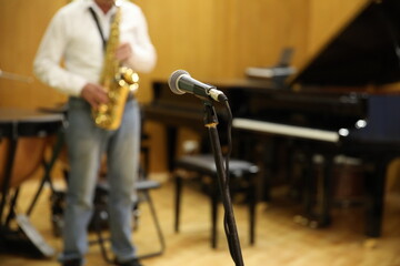 Microphone on a stand close-up on a blurry background, a male saxophonist plays on stage in blue jeans and a white shirt.Solo performance on the musical instrument golden saxophone