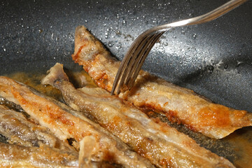 Fried fish in a frying pan. Small crispy fish are fried in oil. Shallow depth of field