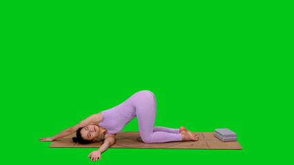 Young sporty woman in bodysuit doing twisted puppy pose while practicing yoga on green screen...