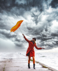 A girl with an orange umbrella in stormy weather on the pier.