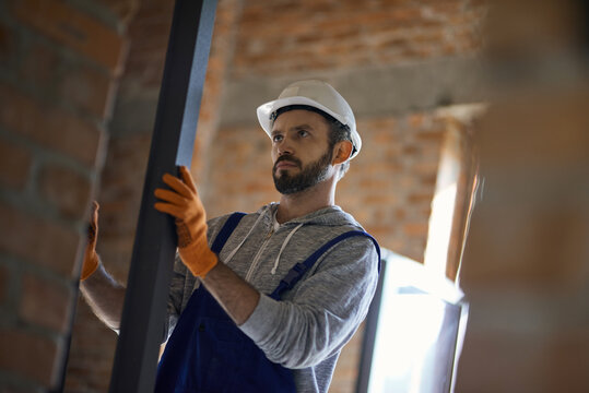 Focused young male builder wearing hard hat holding metal stud for drywall while working at construction site