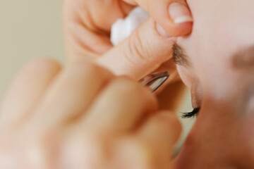 Young caucasian woman getting her eyebrows plucked by her beautician using tweezers. Shallow depth of field, focus on the eyelid