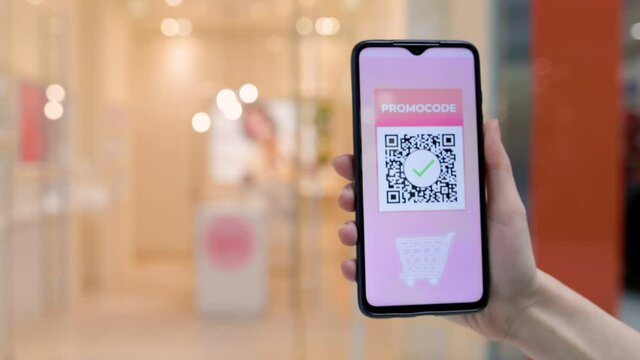 A female's hand shows a smartphone with a promo code for a discount on a purchase in an online store. Blurred background. Close up. The concept of ecommerce and consumerism.
