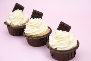  Set  cupcakes with vanilla cream decorated with  pink beads  and chocolate on pink background with  copy space for text .