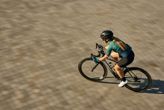 High angle view shot of professional female cyclist in cycling garment and protective gear looking focused while riding bicycle, training outdoors on a daytime