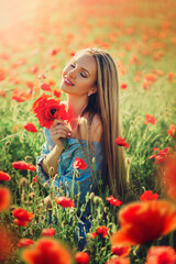 Naklejka premium Beautiful young woman walks in a field with poppy flowers at sunset.
