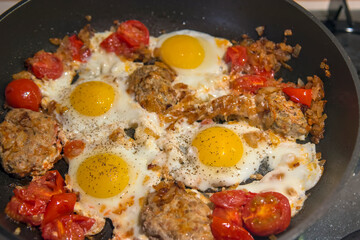 Fried eggs with onions, spices, tomatoes and homemade cutlets in a frying pan. Selective focus.