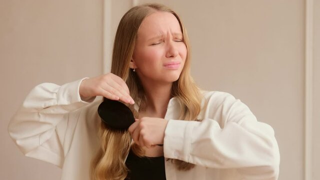A woman has problems combing brushing her dry damaged hair with difficulty. Hard to style tangled hair.