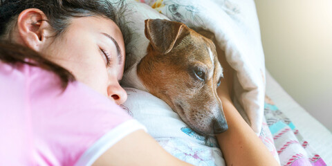 schoolgirl sleeps on bed hugging brown dog under blanket
