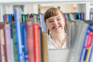 Girl with syndrome down chooses a book on a shelf in the library. Education for disabled children concept