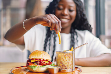 African woman with afro hair eating a tasty classic burger with fries.