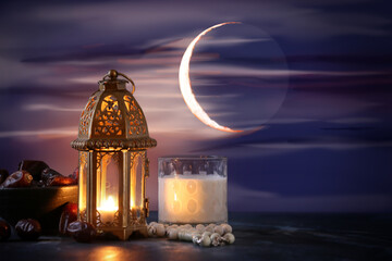Muslim lamp, glass of milk and tasbih with dates on table against night sky