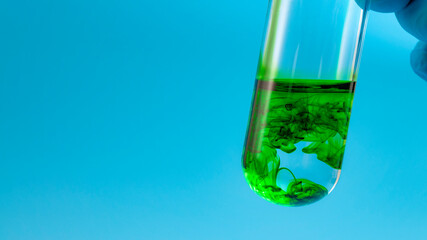 Laboratory safety, chemical analysis and scientific experiment concept with lab technical or scientist hand holding test tube with green liquid isolated on blue background with copy space